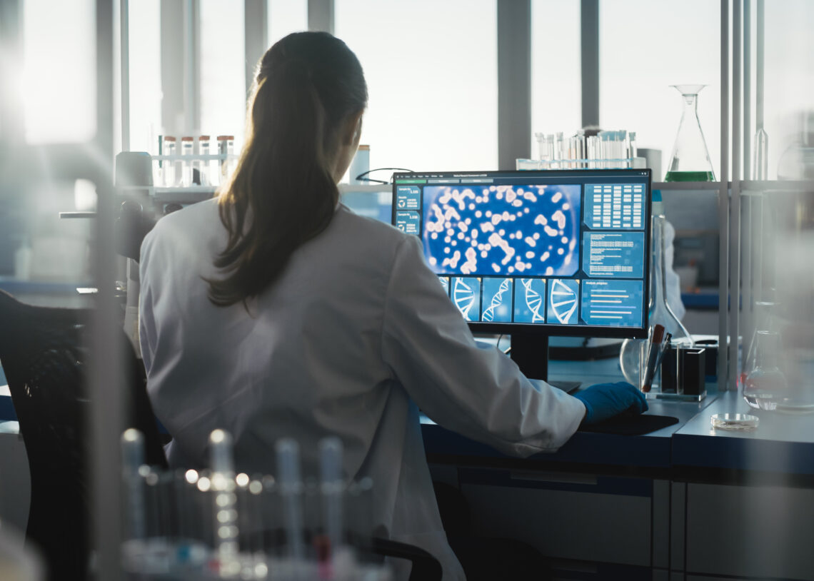 Researcher in a lab coat viewing biological data on a computer screen in a laboratory